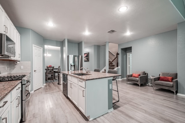 kitchen with white cabinetry, a kitchen island with sink, appliances with stainless steel finishes, and dark stone counters