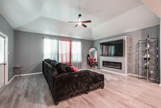 living room with ceiling fan, a large fireplace, wood-type flooring, and vaulted ceiling