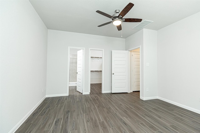 unfurnished bedroom with a walk in closet, ceiling fan, a closet, and dark wood-type flooring