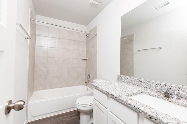 full bathroom with hardwood / wood-style floors, vanity, tiled shower / bath combo, and toilet