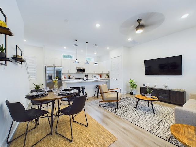 dining space with ceiling fan, sink, and light wood-type flooring