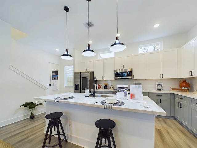 kitchen featuring hanging light fixtures, gray cabinets, light wood-type flooring, an island with sink, and stainless steel appliances