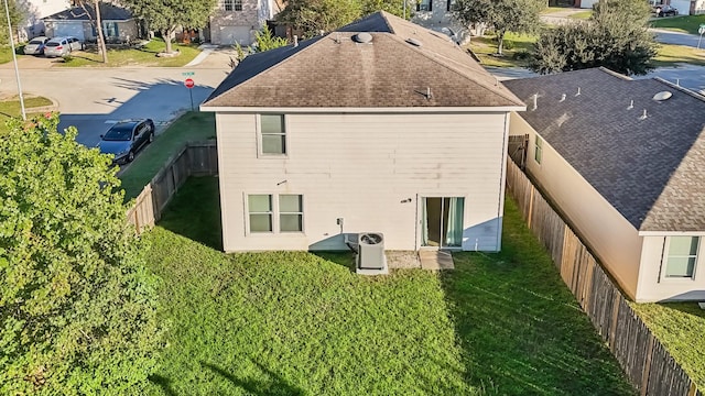 rear view of house featuring a fenced backyard, a shingled roof, and a lawn