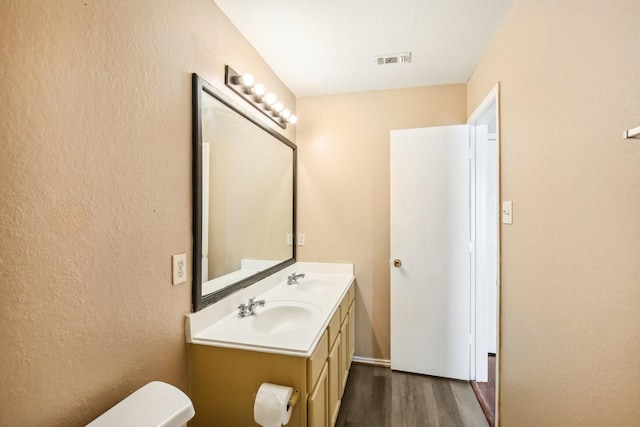 bathroom with toilet, visible vents, a sink, and wood finished floors