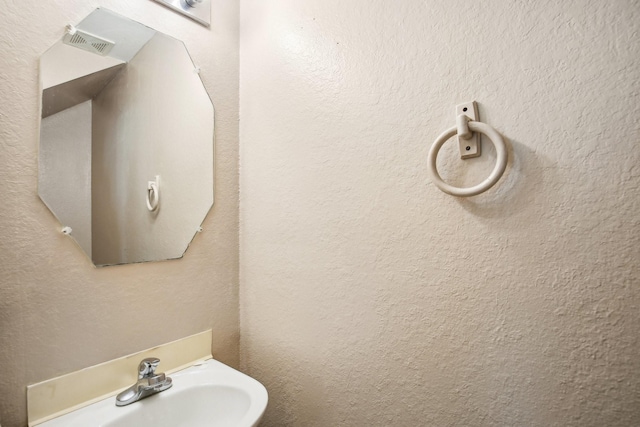 bathroom with a textured wall, visible vents, and a sink