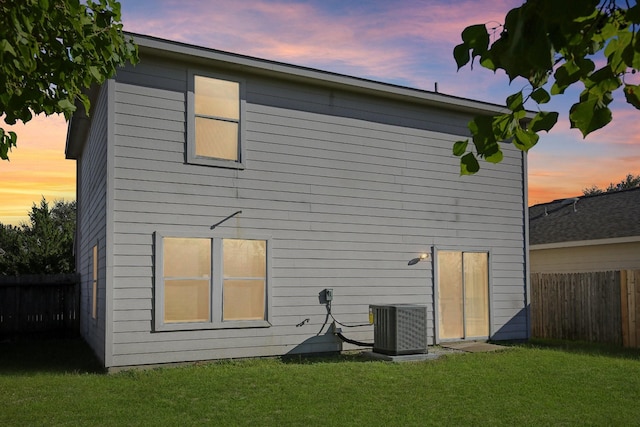 back of property at dusk featuring a fenced backyard, central AC, and a yard