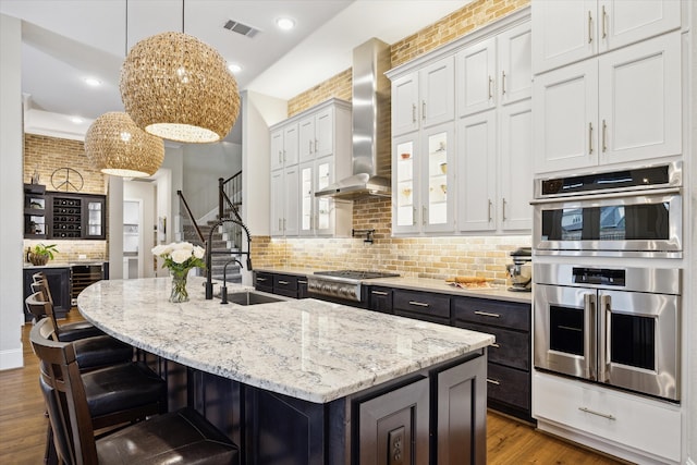 kitchen featuring a kitchen breakfast bar, a center island with sink, stainless steel appliances, and wall chimney range hood