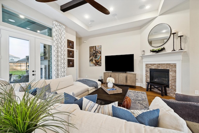 living room featuring ceiling fan, french doors, a brick fireplace, beamed ceiling, and hardwood / wood-style flooring