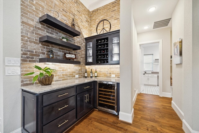 bar with light stone countertops, dark hardwood / wood-style flooring, beverage cooler, and backsplash