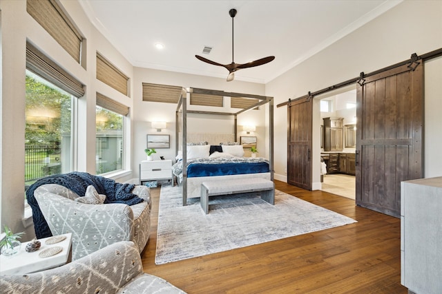 bedroom with dark hardwood / wood-style flooring, ceiling fan, crown molding, a barn door, and connected bathroom