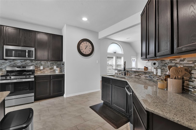 kitchen featuring sink, stainless steel appliances, tasteful backsplash, light stone counters, and dark brown cabinets