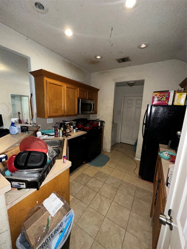 kitchen with black fridge, light tile patterned floors, and a textured ceiling