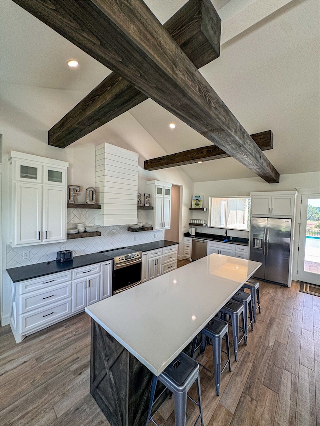 kitchen with lofted ceiling with beams, stainless steel appliances, white cabinetry, and a healthy amount of sunlight