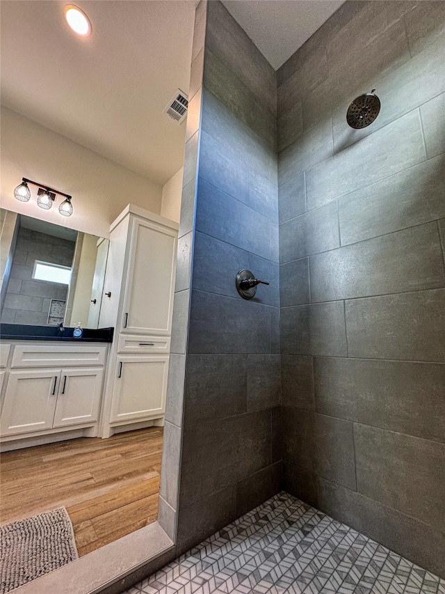 bathroom with vanity, a tile shower, and wood-type flooring