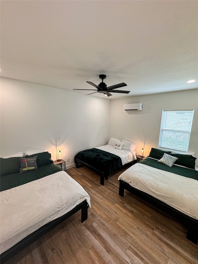 bedroom with a wall mounted AC, wood-type flooring, and ceiling fan