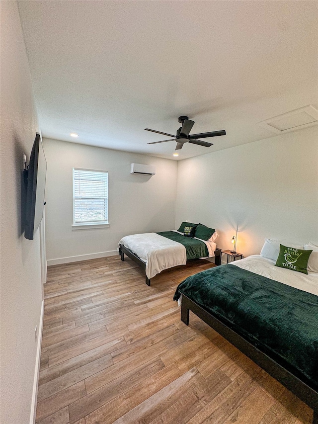 bedroom with light hardwood / wood-style flooring, ceiling fan, and a wall unit AC