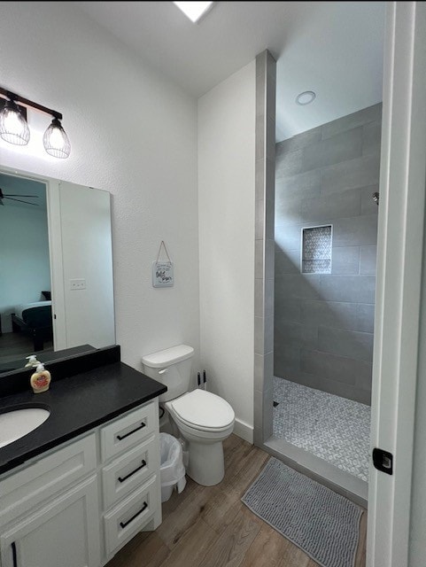 bathroom with hardwood / wood-style flooring, vanity, toilet, and tiled shower