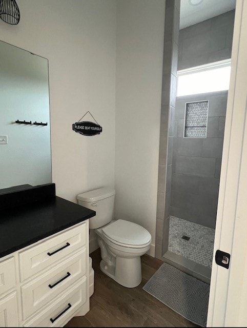 bathroom featuring toilet, wood-type flooring, vanity, and a tile shower