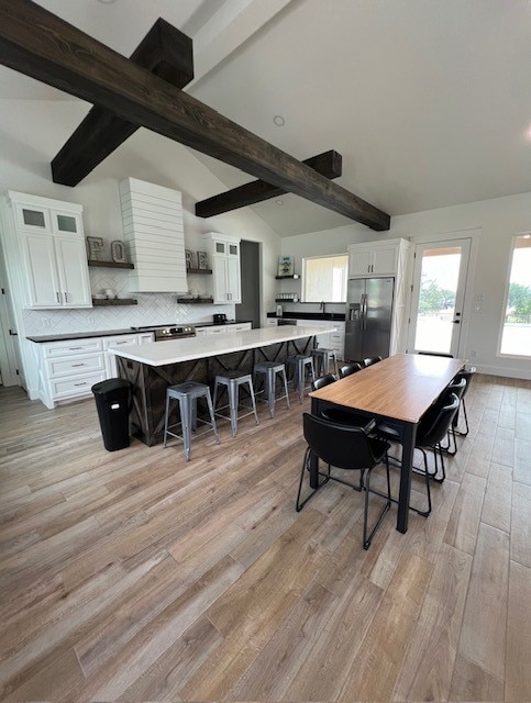 dining space featuring light wood-type flooring and vaulted ceiling with beams