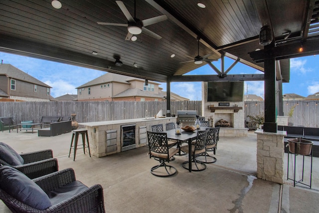 view of patio / terrace featuring exterior bar, an outdoor stone fireplace, ceiling fan, exterior kitchen, and a grill