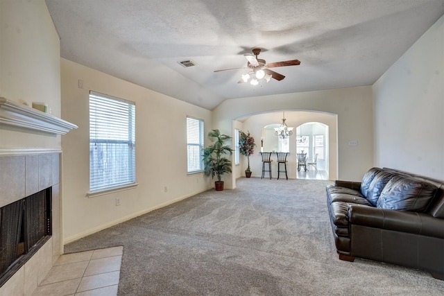 carpeted living room with vaulted ceiling, a tile fireplace, ceiling fan, and a textured ceiling