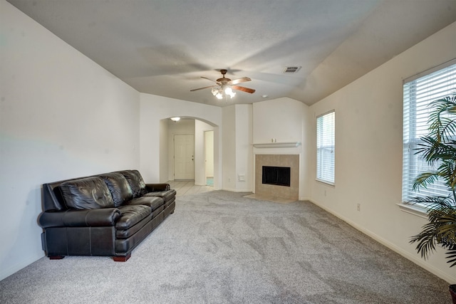 living room with a tile fireplace, light colored carpet, vaulted ceiling, and ceiling fan