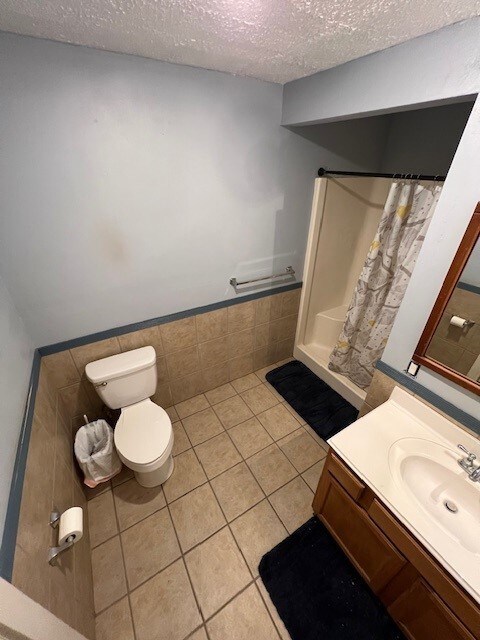 bathroom featuring walk in shower, tile patterned flooring, a textured ceiling, toilet, and vanity