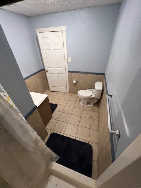 bathroom featuring tile patterned floors, toilet, tile walls, and a textured ceiling