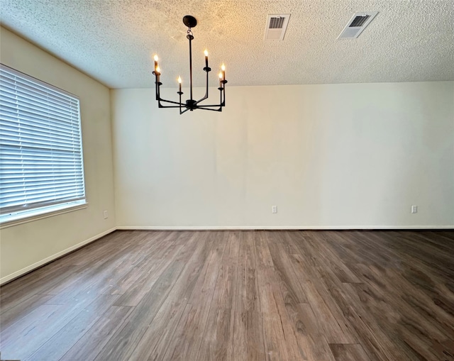 unfurnished dining area with a textured ceiling, hardwood / wood-style flooring, and an inviting chandelier