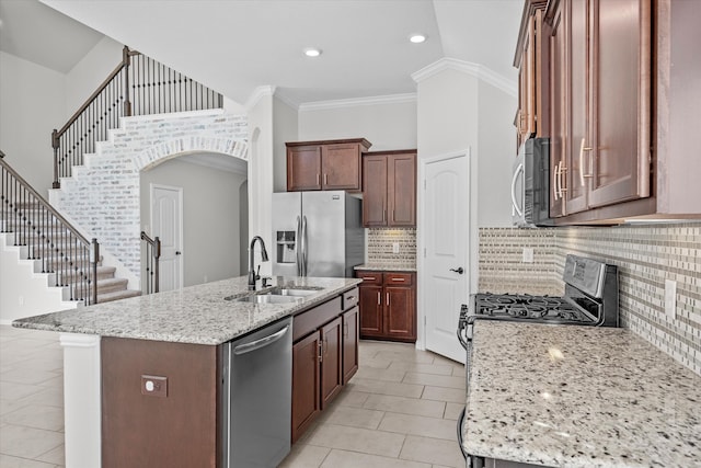 kitchen with light stone countertops, decorative backsplash, stainless steel appliances, sink, and an island with sink