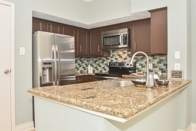 kitchen featuring decorative backsplash, light stone counters, kitchen peninsula, and appliances with stainless steel finishes