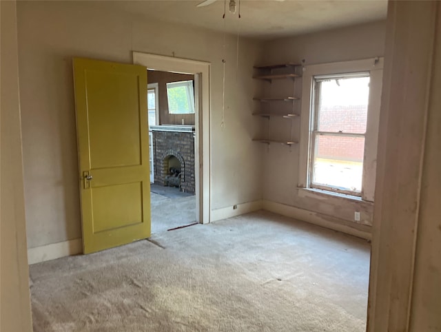 carpeted empty room with ceiling fan and a fireplace