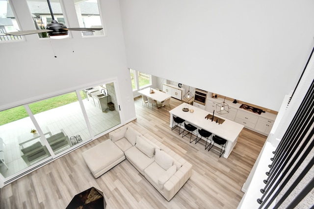 living room with a towering ceiling, light hardwood / wood-style floors, and ceiling fan