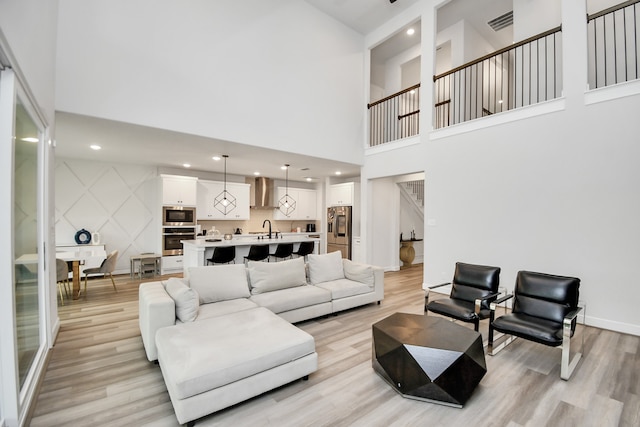 living room with light wood-type flooring, a towering ceiling, and sink