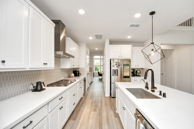 kitchen featuring white cabinets, wall chimney range hood, hanging light fixtures, sink, and appliances with stainless steel finishes