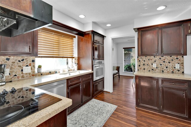 kitchen with ventilation hood, tasteful backsplash, dark hardwood / wood-style flooring, dark brown cabinetry, and stainless steel appliances