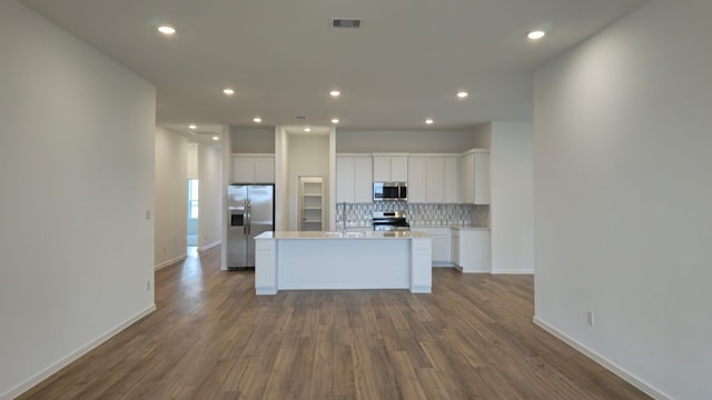 kitchen with visible vents, an island with sink, appliances with stainless steel finishes, white cabinets, and decorative backsplash