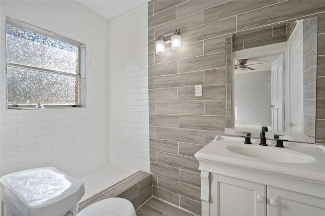 bathroom featuring a tile shower, ceiling fan, vanity, and tile walls