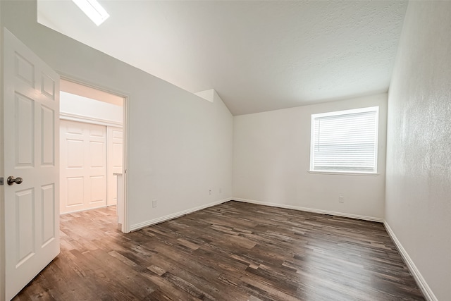 empty room with dark hardwood / wood-style floors, lofted ceiling with skylight, and a textured ceiling