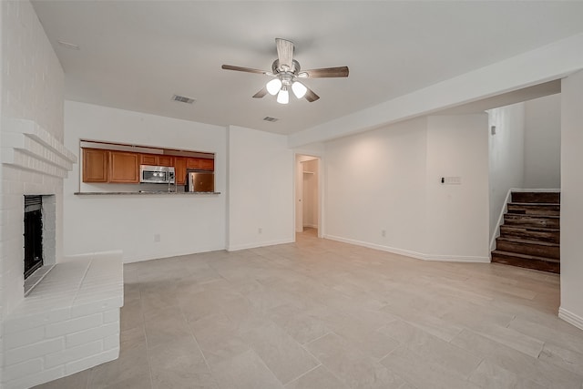 unfurnished living room featuring ceiling fan and a brick fireplace