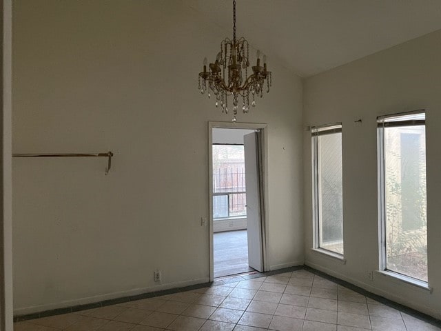 tiled empty room featuring a healthy amount of sunlight, lofted ceiling, and an inviting chandelier