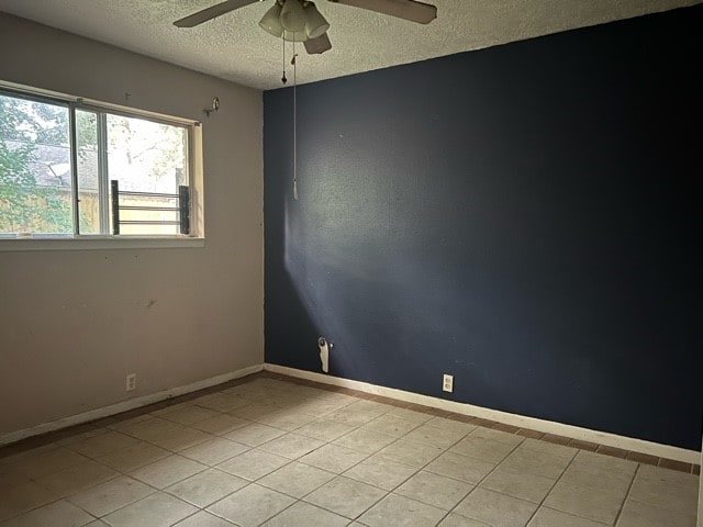 unfurnished room featuring ceiling fan, light tile patterned flooring, and a textured ceiling