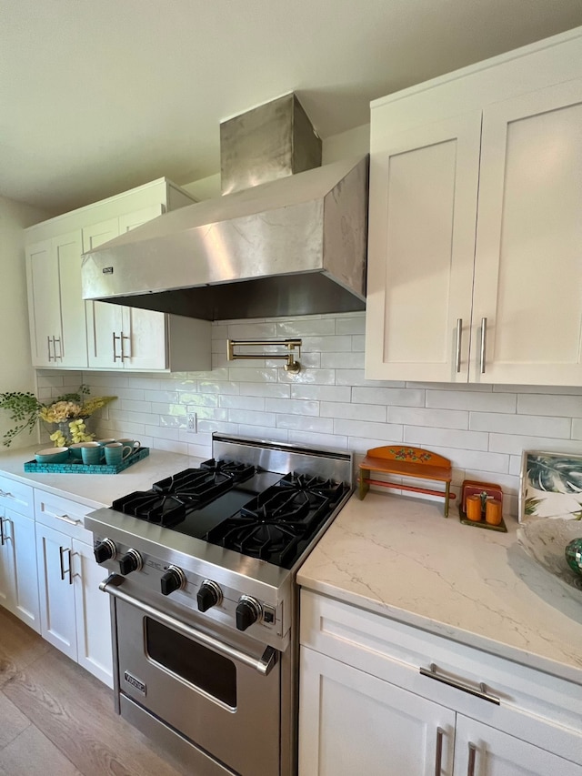 kitchen featuring high end range, light stone counters, wall chimney range hood, light hardwood / wood-style flooring, and white cabinets