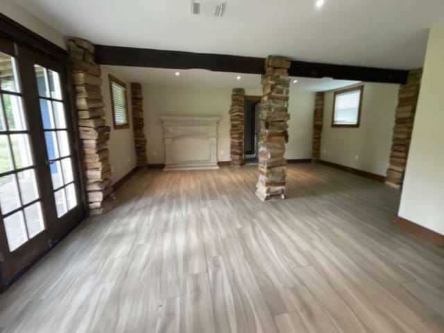 unfurnished living room with french doors, light wood-type flooring, decorative columns, and plenty of natural light