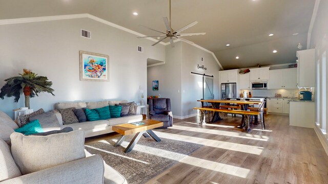 living room featuring ceiling fan, a barn door, high vaulted ceiling, crown molding, and light wood-type flooring