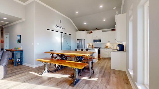 dining space with a barn door, crown molding, light hardwood / wood-style flooring, and high vaulted ceiling