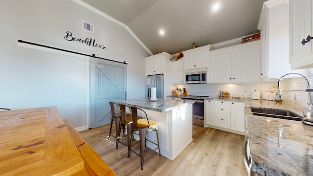 kitchen featuring white cabinetry, a center island, a barn door, light stone counters, and appliances with stainless steel finishes