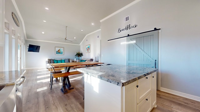 kitchen with light stone countertops, a center island, a barn door, light hardwood / wood-style flooring, and lofted ceiling