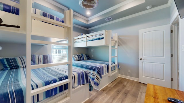 bedroom with a raised ceiling, ornamental molding, and light wood-type flooring