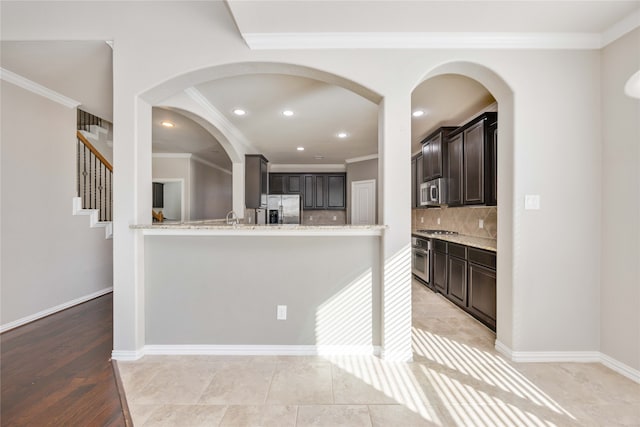 kitchen featuring light stone countertops, dark brown cabinets, stainless steel appliances, and ornamental molding